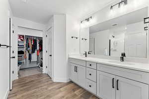 Full bathroom featuring a spacious closet, double vanity, a shower stall, light wood-style floors, and a textured ceiling