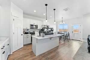 Kitchen featuring white cabinets, a kitchen island with sink, decorative light fixtures, stainless steel appliances, and dark wood-style flooring