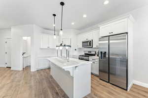 Kitchen with appliances with stainless steel finishes, white cabinetry, hanging light fixtures, an island with sink, and recessed lighting