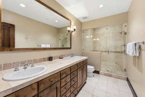 Full bath with double vanity, a shower stall, light tile patterned floors, and recessed lighting