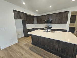 Kitchen with dark brown cabinets, a center island with sink, light stone countertops, tasteful backsplash, and stainless steel appliances