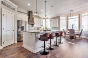 Kitchen with stainless steel refrigerator with ice dispenser, white cabinetry, light stone countertops, decorative light fixtures, and decorative backsplash