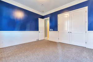 Unfurnished bedroom with wainscoting, a closet, and crown molding