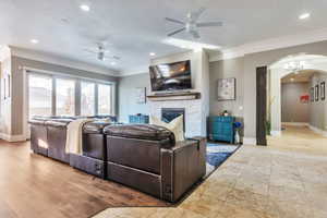 Living room with arched walkways, a high end fireplace, a ceiling fan, recessed lighting, and crown molding