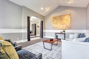 Carpeted living area with arched walkways and vaulted ceiling