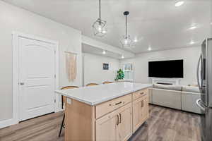 Kitchen featuring light brown cabinetry, a breakfast bar area, open floor plan, a kitchen island, and freestanding refrigerator