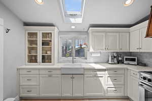 Kitchen featuring a skylight, white cabinetry, high end stainless steel range, decorative backsplash, and recessed lighting