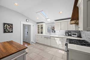 Kitchen featuring stainless steel gas stove, lofted ceiling, white cabinets, a skylight, and recessed lighting