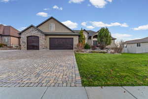 View of front of house with stucco siding, decorative driveway, stone siding, and an attached garage