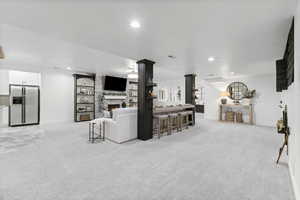 Living room featuring a stone fireplace, light carpet, recessed lighting, bar area, and built in features
