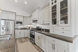 Kitchen with stainless steel appliances, white cabinets, light wood finished floors, dark stone counters, and glass insert cabinets