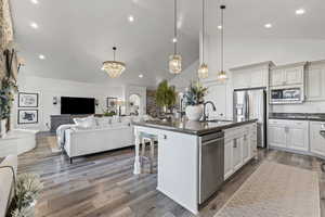 Kitchen featuring high vaulted ceiling, decorative light fixtures, appliances with stainless steel finishes, dark stone countertops, and open floor plan