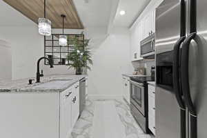 Kitchen with appliances with stainless steel finishes, white cabinets, hanging light fixtures, light stone counters, and light marble finish flooring