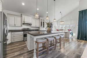 Kitchen with appliances with stainless steel finishes, hanging light fixtures, a breakfast bar area, an island with sink, and dark stone countertops