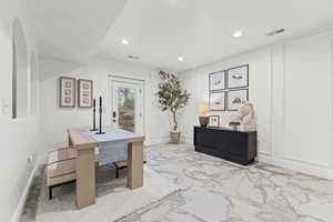 Office area featuring a decorative wall, marble tiled flooring, and recessed lighting