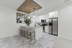 Kitchen featuring a breakfast bar, stainless steel appliances, a peninsula, light stone counters, and white cabinetry