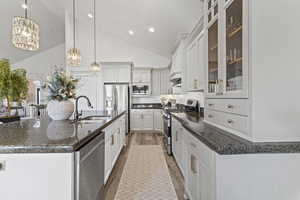 Kitchen featuring stainless steel appliances, pendant lighting, glass insert cabinets, high vaulted ceiling, and dark stone counters