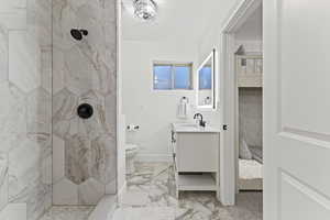 Ensuite bathroom featuring vanity, a marble finish shower, and light marble finish floors