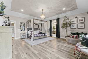 Bedroom with a raised ceiling, light wood-style floors, recessed lighting, and a chandelier