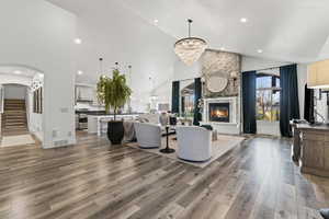 Living area featuring arched walkways, a stone fireplace, light wood-type flooring, a chandelier, and recessed lighting