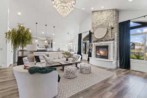 Living area featuring light wood-style floors, a fireplace, high vaulted ceiling, healthy amount of natural light, and a chandelier