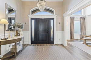 Foyer entrance featuring wood-type flooring, a chandelier, and a wainscoted wall