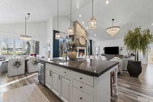 Kitchen with open floor plan, a chandelier, white cabinets, high vaulted ceiling, and a fireplace