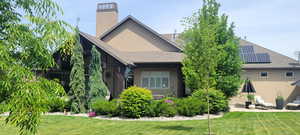 Rear view of property with a lawn, a chimney, stucco siding, and a shingled roof