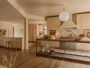 Kitchen featuring wall chimney range hood, light wood finished floors, backsplash, and wooden counters