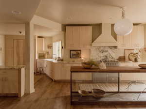 Kitchen with stainless steel range oven, wall chimney range hood, hanging light fixtures, light brown cabinetry, and light stone counters