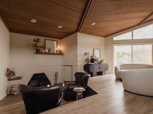 Living room with a warm lit fireplace, vaulted ceiling, wooden ceiling, wood finished floors, and brick wall