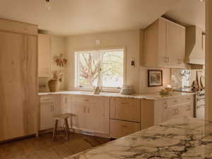 Kitchen featuring wall chimney exhaust hood, light brown cabinets, electric stove, wood finished floors, and light stone countertops