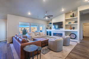 Living area featuring wood finished floors, a fireplace, built in features, lofted ceiling, and a ceiling fan