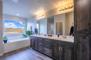 Bathroom with double vanity, a garden tub, light wood-style floors, and recessed lighting