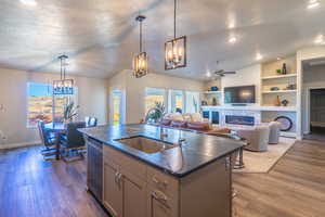 Kitchen featuring built in shelves, decorative light fixtures, an island with sink, a chandelier, and lofted ceiling