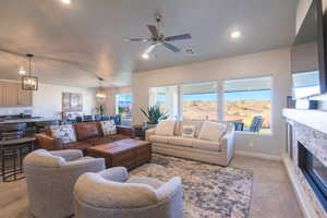 Living room featuring light colored carpet, a ceiling fan, a stone fireplace, recessed lighting, and a chandelier