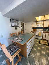 Kitchen with a kitchen bar, brown cabinets, white cabinets, white appliances, and a textured ceiling