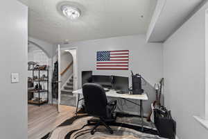 Home office featuring a textured ceiling, arched walkways, and light wood finished floors