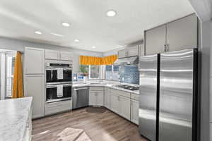 Kitchen featuring stainless steel appliances, gray cabinets, light wood-style floors, backsplash, and recessed lighting