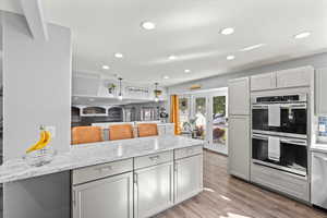 Kitchen featuring appliances with stainless steel finishes, light stone countertops, recessed lighting, light wood-style flooring, and gray cabinets