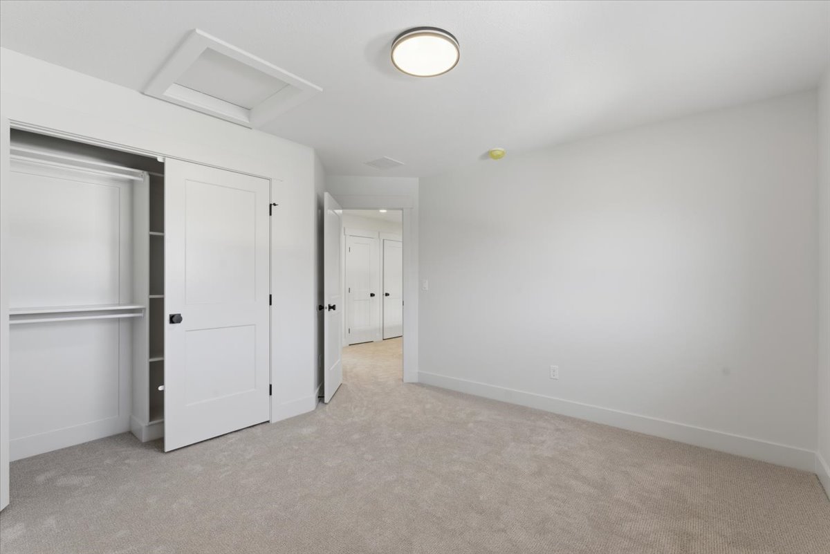 Unfurnished bedroom with attic access, light colored carpet, and a closet