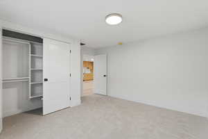 Unfurnished bedroom featuring light carpet and a closet