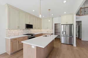 Kitchen with appliances with stainless steel finishes, an island with sink, decorative backsplash, decorative light fixtures, and light wood-style flooring