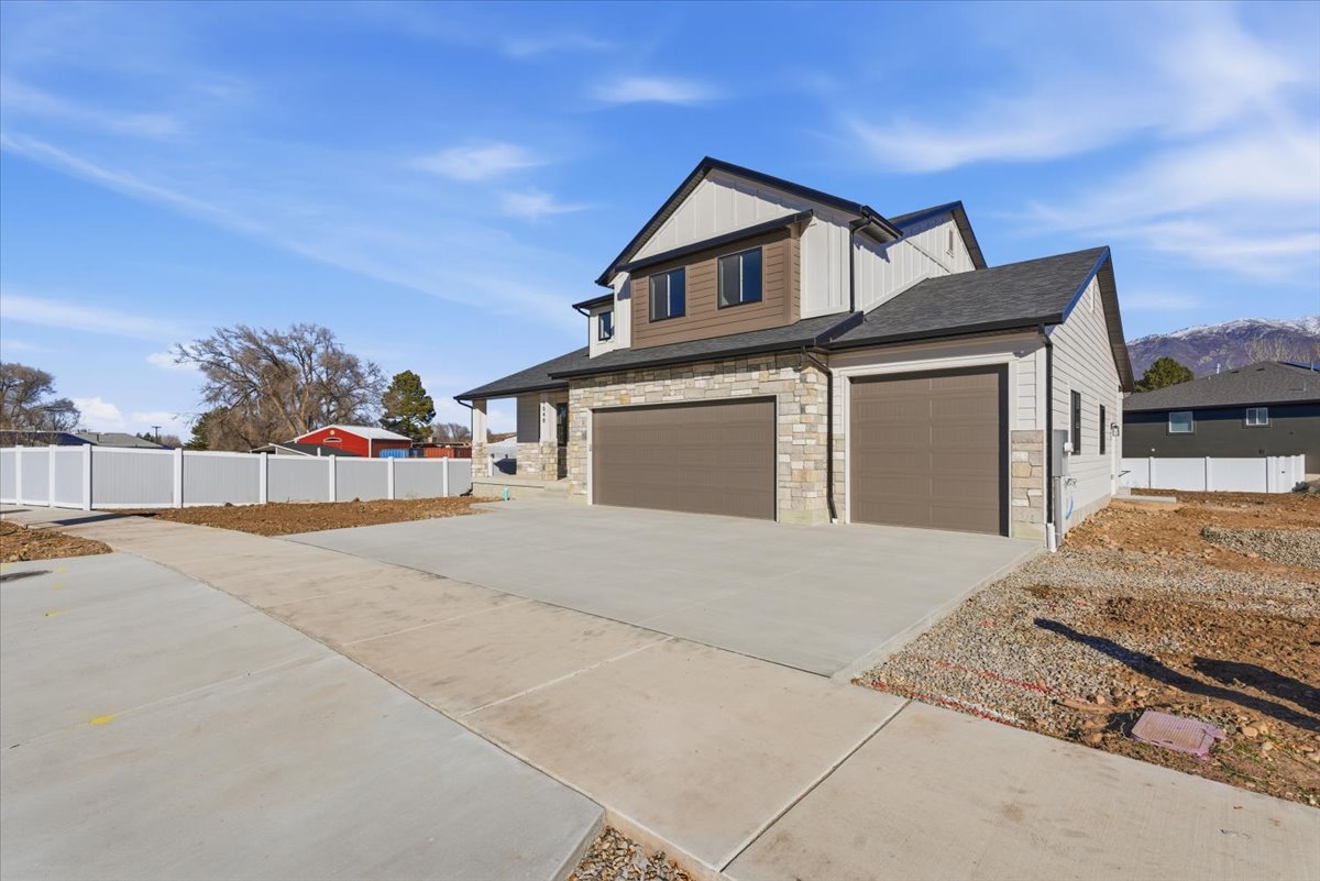 View of front facade featuring board and batten siding, concrete driveway, stone siding, and a garage