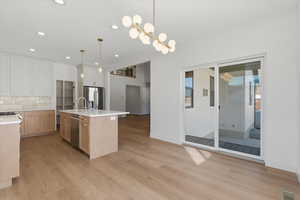 Kitchen with pendant lighting, a center island with sink, light stone counters, light wood finished floors, and recessed lighting