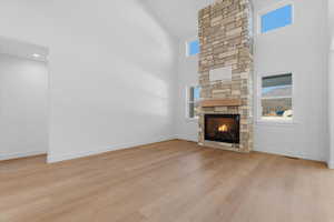 Unfurnished living room featuring a high ceiling, a stone fireplace, light wood-style floors, and plenty of natural light