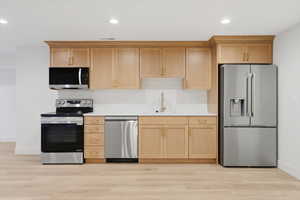 Kitchen featuring appliances with stainless steel finishes, light brown cabinetry, light wood-type flooring, and recessed lighting