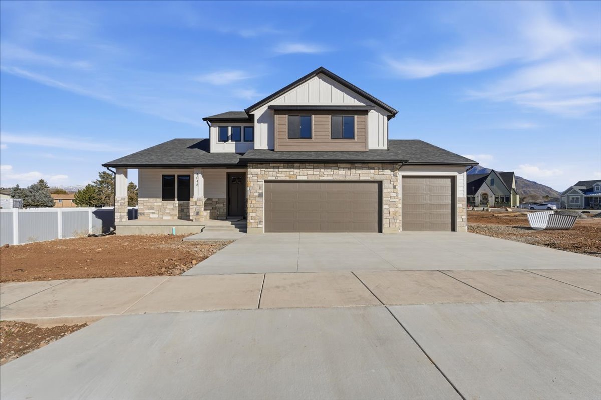View of front of home featuring stone siding, covered porch, concrete driveway, board and batten siding, and an attached garage