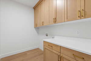 Laundry area with washer hookup, light wood-style flooring, and cabinet space