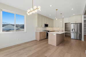 Kitchen with stainless steel appliances, pendant lighting, a kitchen island with sink, light stone countertops, and light wood-style flooring